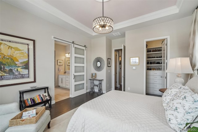 bedroom with ornamental molding, a barn door, a chandelier, wood finished floors, and a raised ceiling