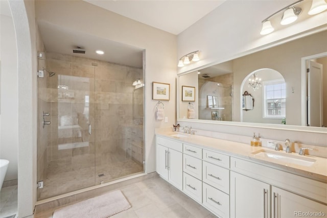 full bathroom with a stall shower, double vanity, a sink, and a notable chandelier