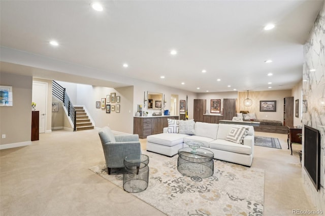 living room with a large fireplace, recessed lighting, light colored carpet, and stairs