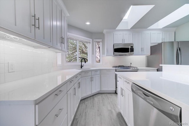 kitchen featuring decorative backsplash, appliances with stainless steel finishes, sink, light hardwood / wood-style flooring, and white cabinetry