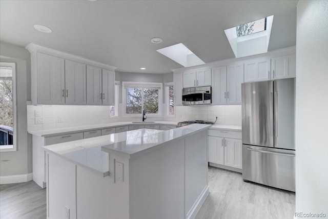 kitchen featuring a skylight, stainless steel appliances, a kitchen island, light hardwood / wood-style flooring, and white cabinets