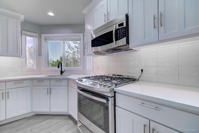 kitchen with sink, light hardwood / wood-style flooring, decorative backsplash, white cabinets, and appliances with stainless steel finishes