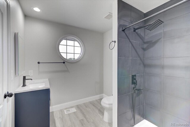 bathroom featuring a tile shower, vanity, hardwood / wood-style flooring, and toilet