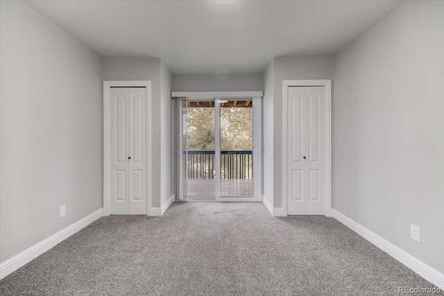 unfurnished bedroom featuring access to outside, carpet floors, and two closets