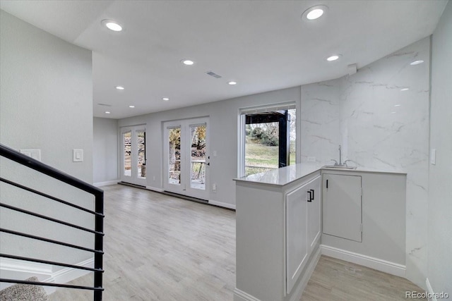 kitchen featuring kitchen peninsula, white cabinetry, sink, and light wood-type flooring