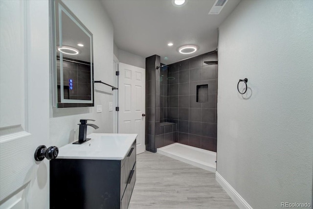 bathroom featuring vanity, a tile shower, and wood-type flooring