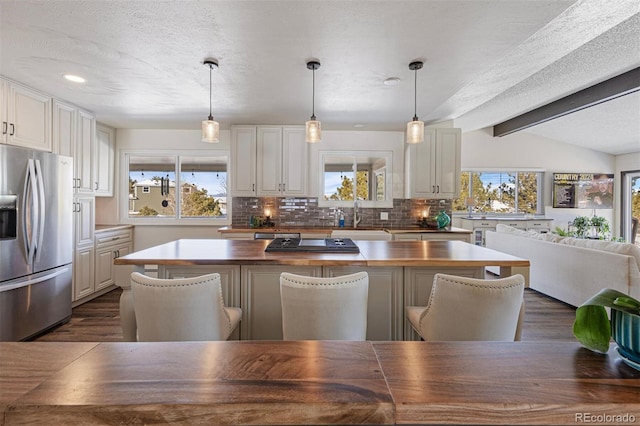 kitchen featuring pendant lighting, lofted ceiling with beams, white cabinets, backsplash, and stainless steel refrigerator with ice dispenser