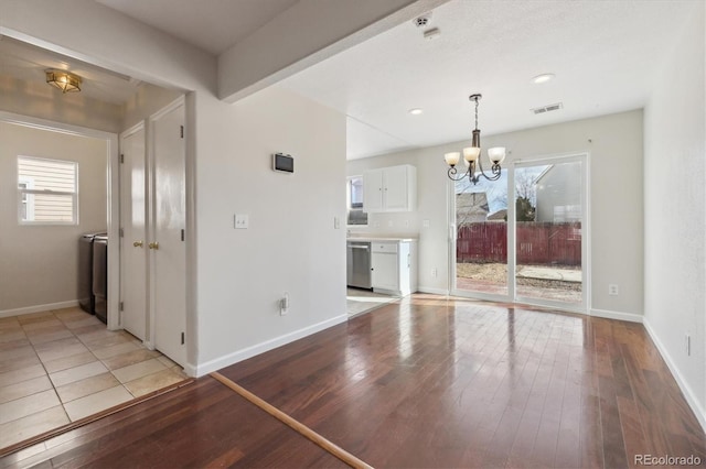 unfurnished living room with visible vents, a notable chandelier, light wood-style flooring, and baseboards