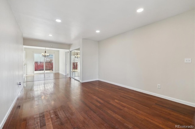 empty room featuring baseboards, dark wood-type flooring, a notable chandelier, and recessed lighting