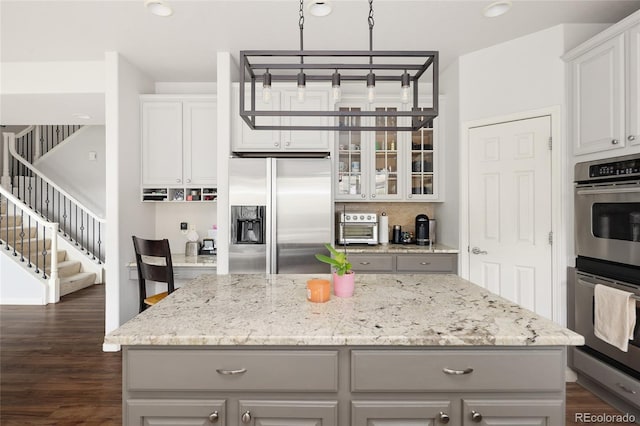 kitchen with white cabinetry, hanging light fixtures, a kitchen island, stainless steel appliances, and light stone countertops