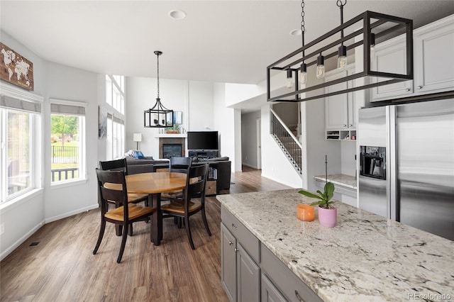 kitchen featuring stainless steel refrigerator with ice dispenser, light stone counters, decorative light fixtures, gray cabinets, and hardwood / wood-style floors