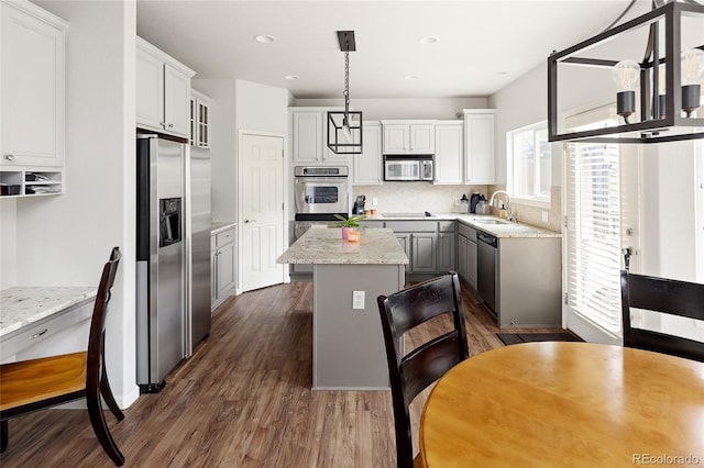 kitchen with appliances with stainless steel finishes, hanging light fixtures, a center island, light stone counters, and dark wood-type flooring