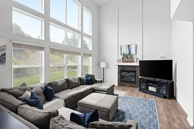 living room featuring a towering ceiling, a healthy amount of sunlight, a tiled fireplace, and hardwood / wood-style floors