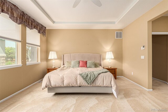 bedroom featuring a raised ceiling, ceiling fan, and light colored carpet