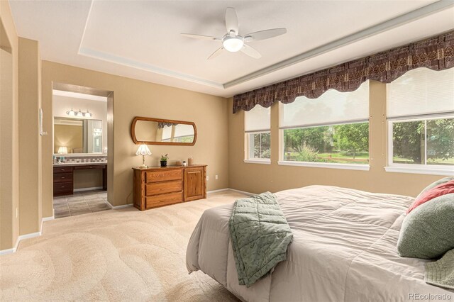 bedroom featuring ceiling fan, light colored carpet, a tray ceiling, and ensuite bathroom