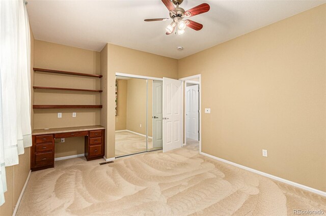 unfurnished bedroom featuring ceiling fan, light colored carpet, a closet, and built in desk