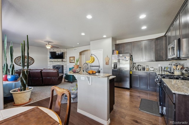 2431 Nicholson St, Berthoud, CO 80513 - kitchen featuring appliances with stainless steel finishes, dark brown cabinets, dark wood-type flooring, open floor plan, and light stone counters