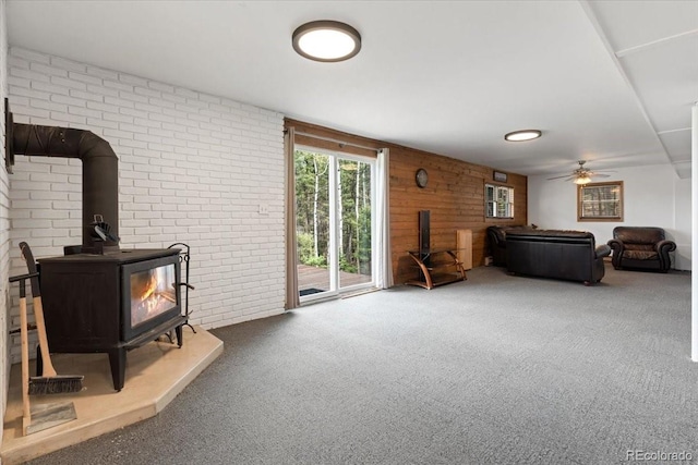 11724 Little Turtle Ln, Conifer, CO 80433 - carpeted living room featuring a wood stove, ceiling fan, brick wall, and wood walls