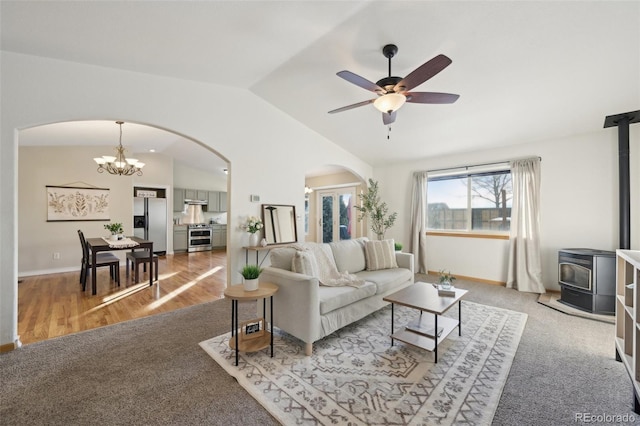 carpeted living room with ceiling fan with notable chandelier, a wood stove, and lofted ceiling