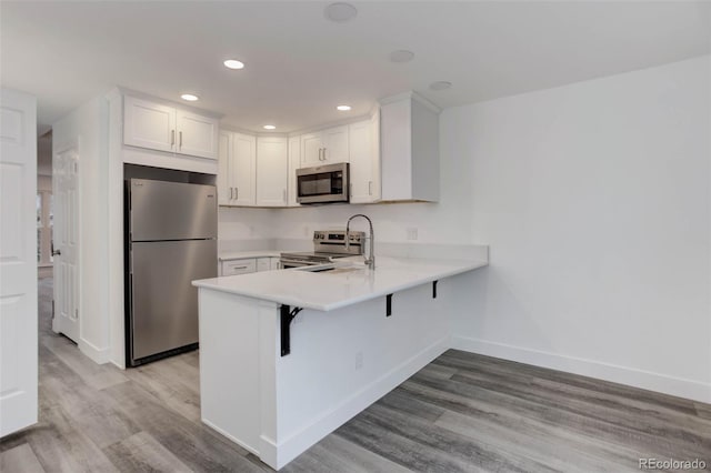 11973 E Kepner Dr, Aurora, CO 80012 - kitchen featuring stainless steel appliances, a peninsula, light wood finished floors, baseboards, and light countertops