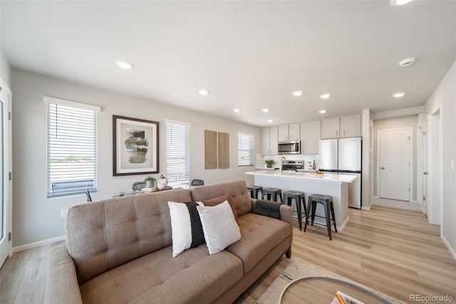 living room with a healthy amount of sunlight, sink, and light hardwood / wood-style flooring