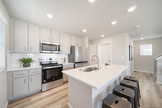 kitchen with appliances with stainless steel finishes, sink, backsplash, a center island with sink, and light hardwood / wood-style flooring