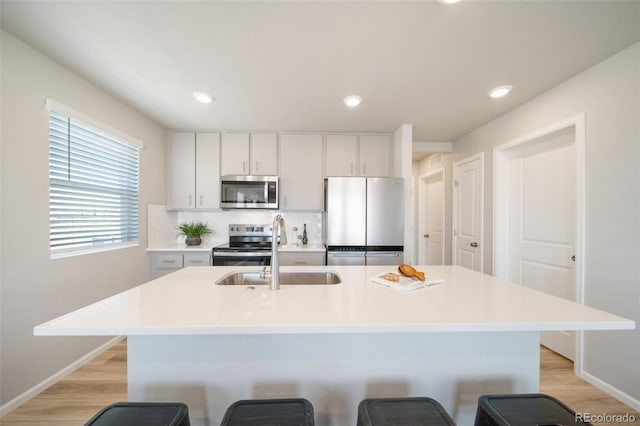 kitchen with a breakfast bar, sink, light hardwood / wood-style flooring, stainless steel appliances, and a kitchen island with sink