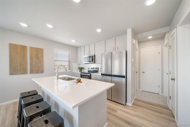 kitchen with an island with sink, sink, white cabinets, a kitchen bar, and stainless steel appliances