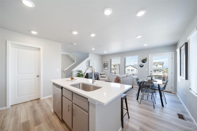 kitchen with sink, an island with sink, dishwasher, and light wood-type flooring