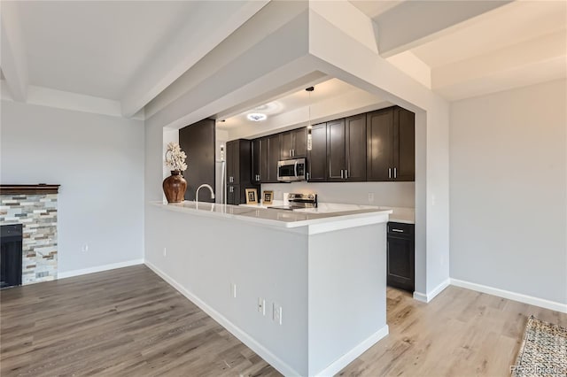 kitchen featuring kitchen peninsula, dark brown cabinets, a fireplace, light hardwood / wood-style floors, and stainless steel appliances