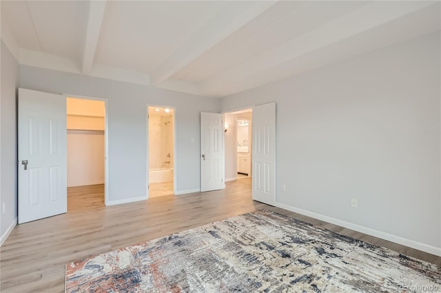 unfurnished bedroom featuring a closet, light hardwood / wood-style flooring, beam ceiling, and a walk in closet