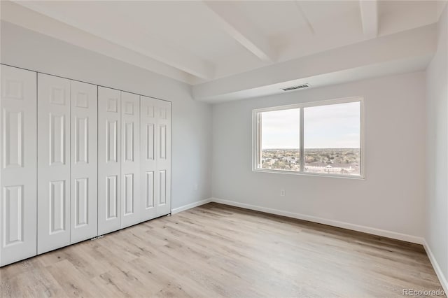 unfurnished bedroom with a closet, light hardwood / wood-style floors, and beam ceiling