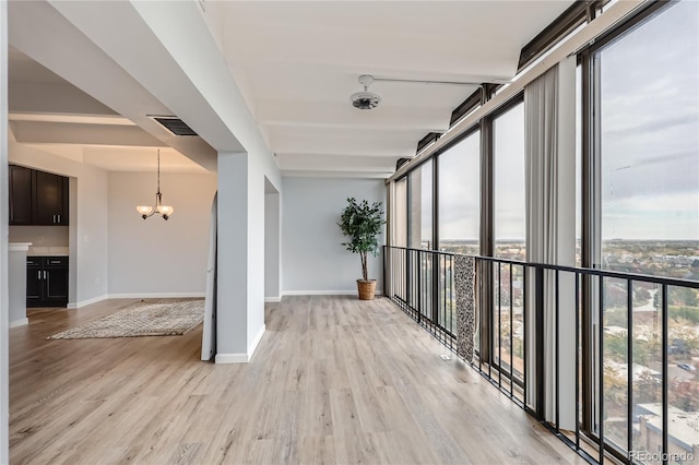 corridor featuring a notable chandelier, a wealth of natural light, and light wood-type flooring