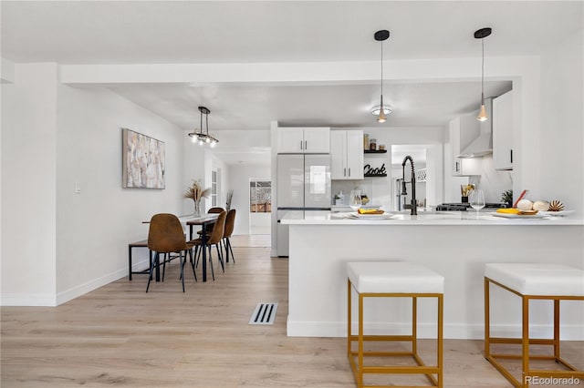 kitchen featuring light hardwood / wood-style flooring, white cabinetry, fridge, decorative light fixtures, and kitchen peninsula