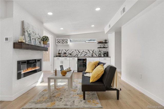 living room featuring light hardwood / wood-style flooring, beverage cooler, and indoor wet bar