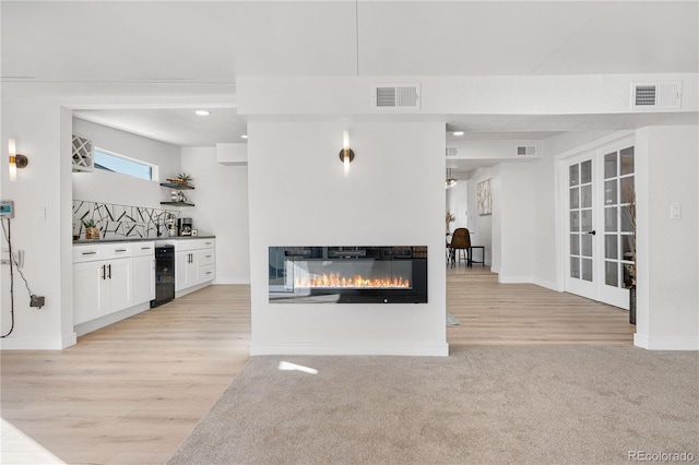 unfurnished living room with wine cooler, light hardwood / wood-style floors, and french doors