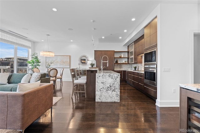 kitchen featuring pendant lighting, a breakfast bar, tasteful backsplash, an island with sink, and dark hardwood / wood-style flooring