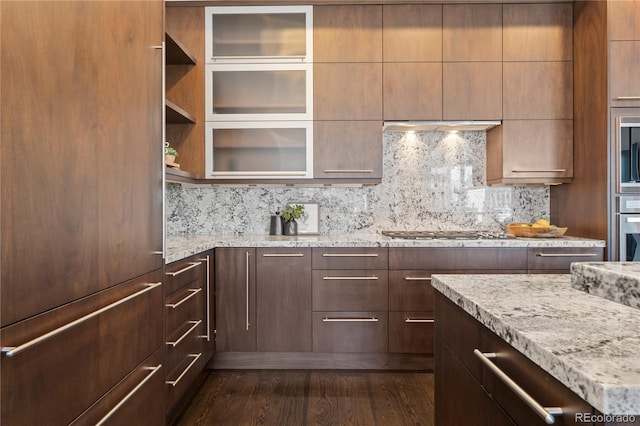 kitchen featuring tasteful backsplash, light stone countertops, dark wood-type flooring, and built in appliances