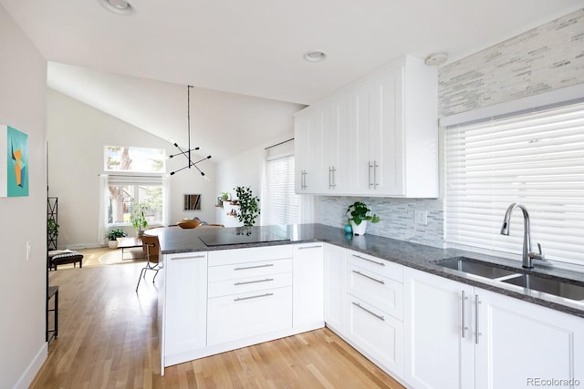 kitchen with a sink, dark stone countertops, a peninsula, and white cabinets