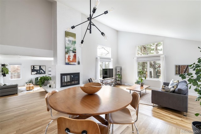 dining area with high vaulted ceiling, a large fireplace, and light wood-style floors