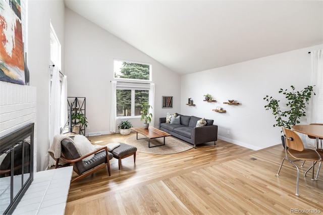living room featuring a brick fireplace, high vaulted ceiling, baseboards, and light wood-type flooring