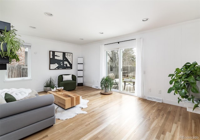 living room featuring baseboards, ornamental molding, wood finished floors, and visible vents