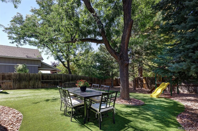 view of yard featuring outdoor dining space, a fenced backyard, and a playground