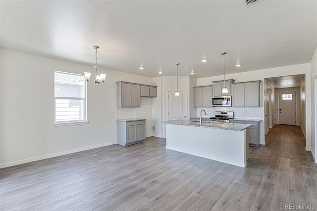 kitchen with light wood finished floors, backsplash, an island with sink, gray cabinets, and stainless steel appliances