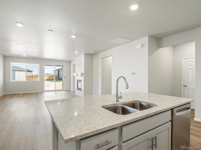 kitchen with sink, light wood-type flooring, stainless steel dishwasher, light stone countertops, and a kitchen island with sink