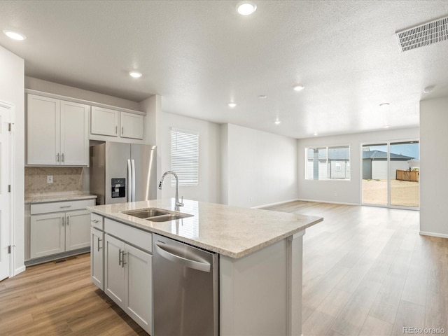 kitchen featuring sink, appliances with stainless steel finishes, an island with sink, light hardwood / wood-style floors, and decorative backsplash