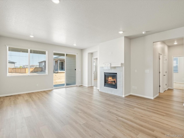 unfurnished living room with light wood-style floors, baseboards, a textured ceiling, and a tiled fireplace