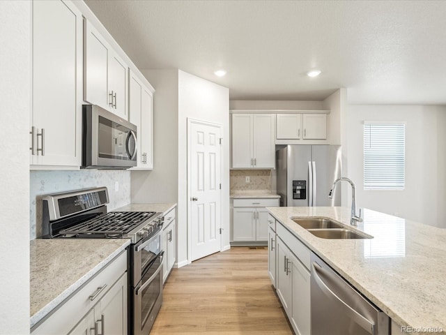 kitchen with tasteful backsplash, light stone counters, stainless steel appliances, light wood-style floors, and a sink