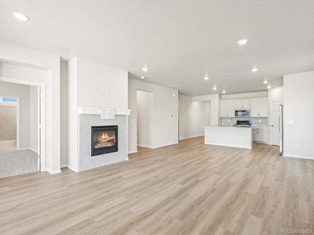 unfurnished living room featuring light wood-type flooring, baseboards, recessed lighting, and a tile fireplace