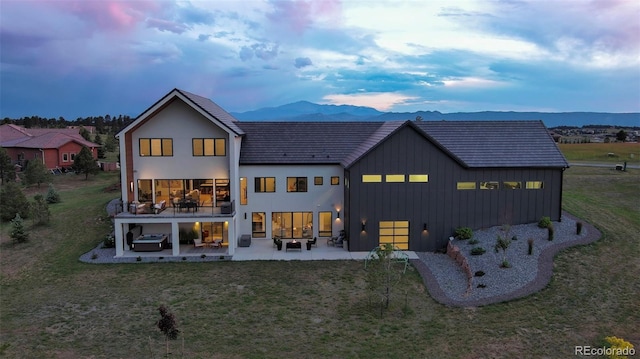 back house at dusk featuring a patio, a mountain view, and a yard